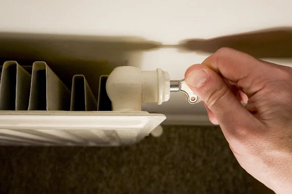 Hand dreht mit Schlüssel Heizkörperventil